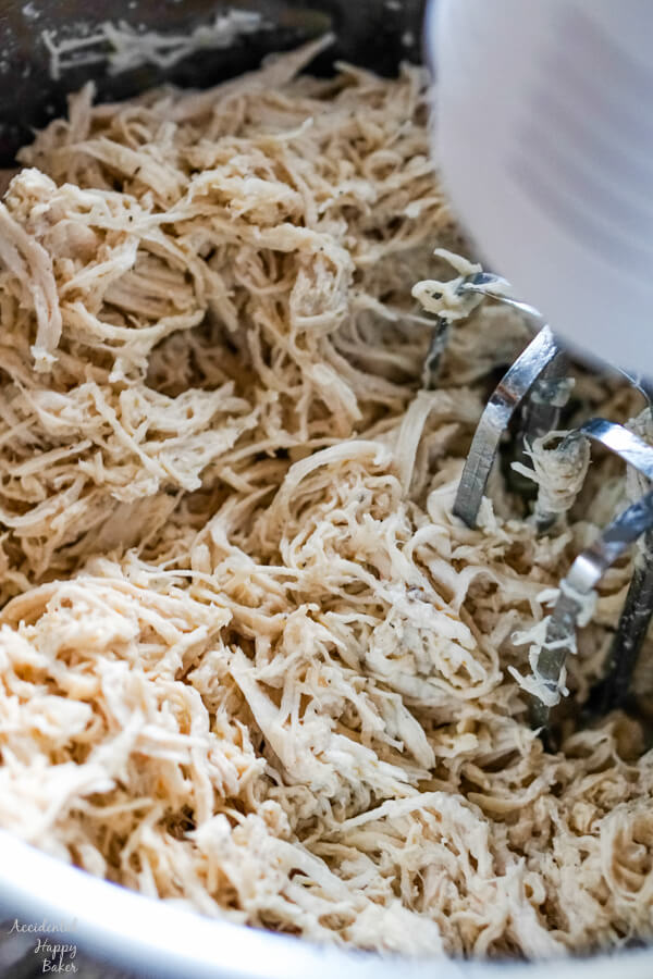 A hand mixer is used to shred the cooked chicken breasts inside the instant pot insert. 