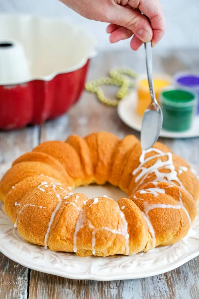 The baked king cake is drizzled with glazed before being decorated with colored sugar. 