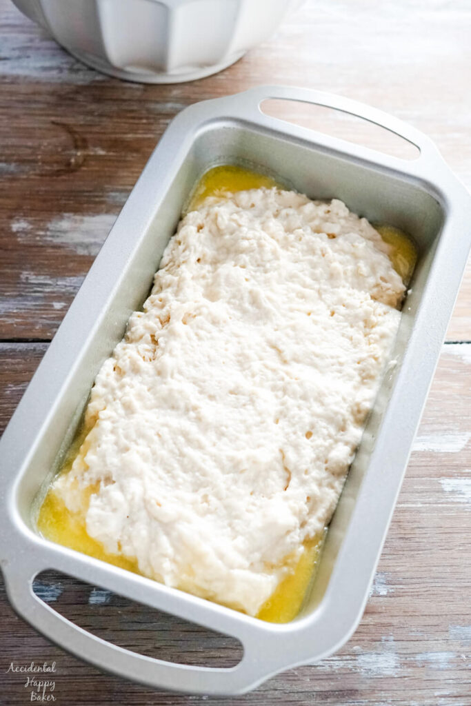 The beer bread batter is spread into a loaf pan that has been coated with melted butter. 