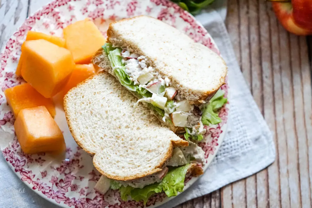 apple pecan chicken salad sandwich with a side of fruit on a floral plate 
