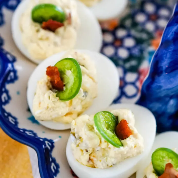 Deviled eggs with a slice of jalapeno and a bit of bacon displayed on a egg plate.