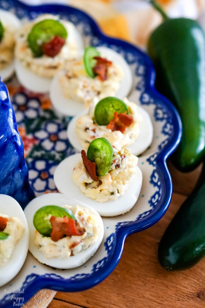 A plate of jalapeno popper deviled eggs garnished with slices of jalapenos sitting next to jalapeno peppers. 