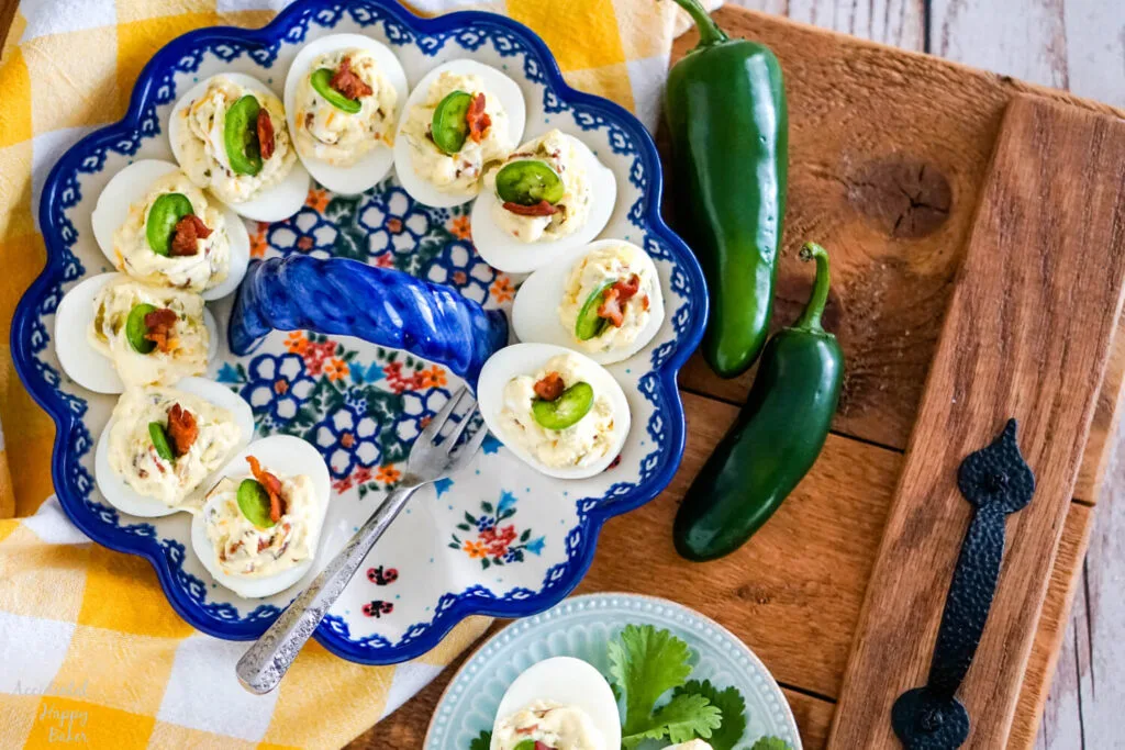 A wooden tray laid with a deviled egg plate, yellow checked towel, and a few fresh jalapeno peppers. 