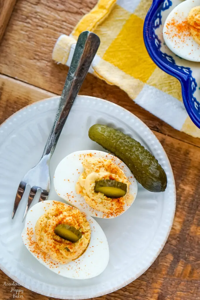 Deviled egg topped with a slice of pickle on a white plate with a fork. 