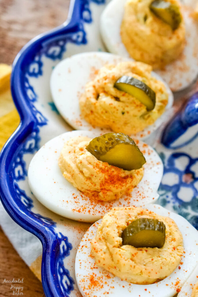 Spicy deviled eggs presented on a deviled egg dish with a slice of pickle on top of each egg.