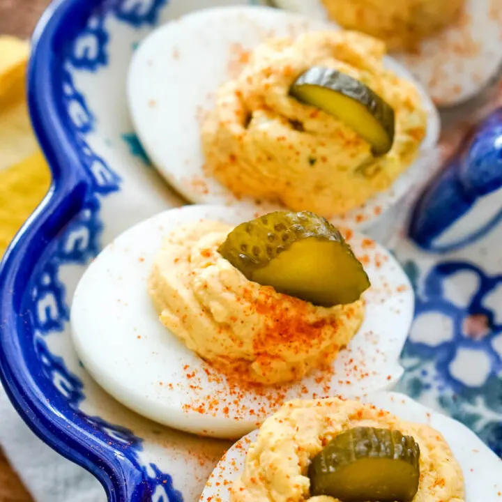 Deviled eggs with a sprinkle of cayenne pepper and a slice of pickle on each egg.
