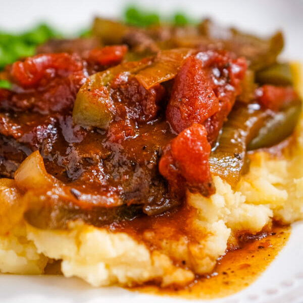 BBQ Swiss Steak with peppers and onions is served up on a pile of cheddar mashed potatoes.