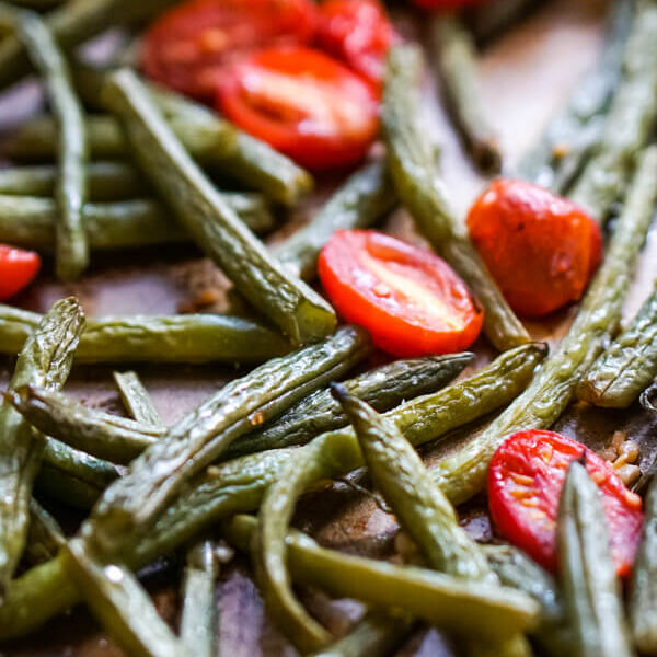 A close up image of a spatula scooping up a serving of roasted green beans and tomatoes.