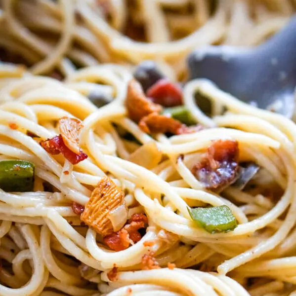 A pan of spaghetti carbonara with a pasta serving scooping out a serving.
