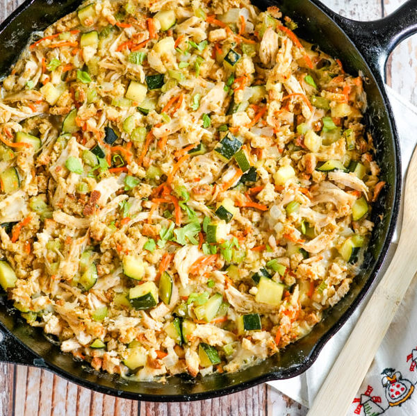 A cast iron skillet full of Chicken Zucchini Casserole sits next to a wooden spoon.