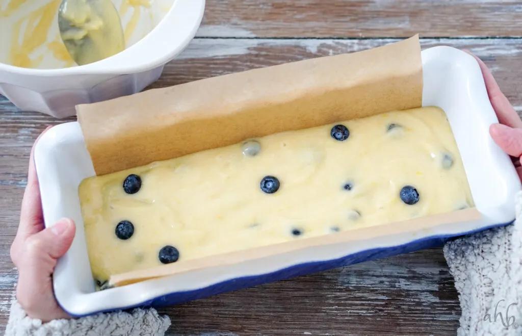 A loaf pan lined with parchment paper and full of lemon blueberry bread batter ready to be placed in the oven. 