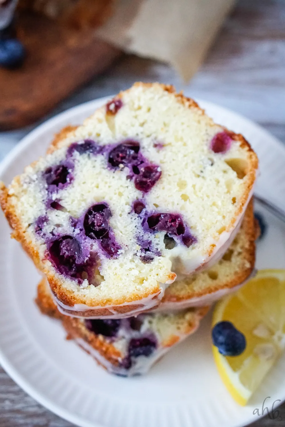 Several slices of lemon blueberry bread on a white plate with a slice of lemon to one side. 