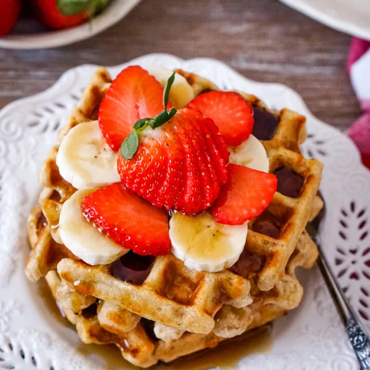 A stack of oatmeal waffles on a white plate with a fork.