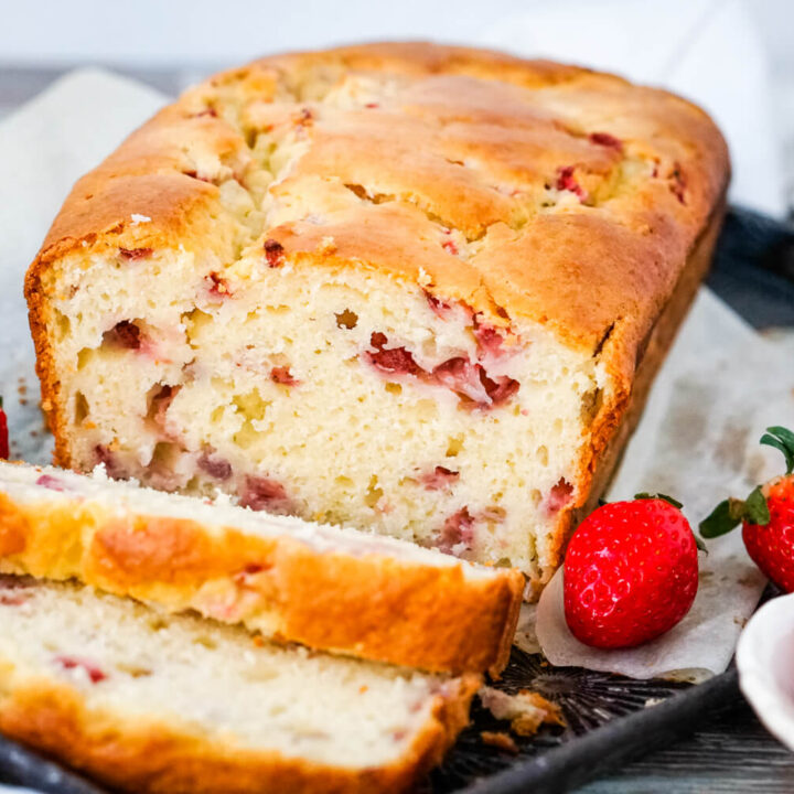 A sliced loaf of Strawberry Bread on a tray with fresh strawberries on each side.