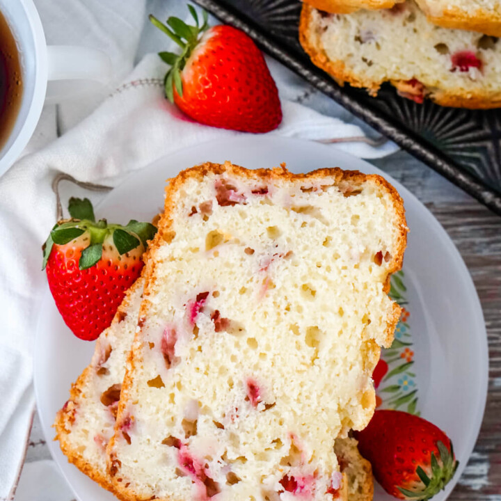 Two Slices of Strawberry Bread on a white plate surrounded by fresh strawberries.