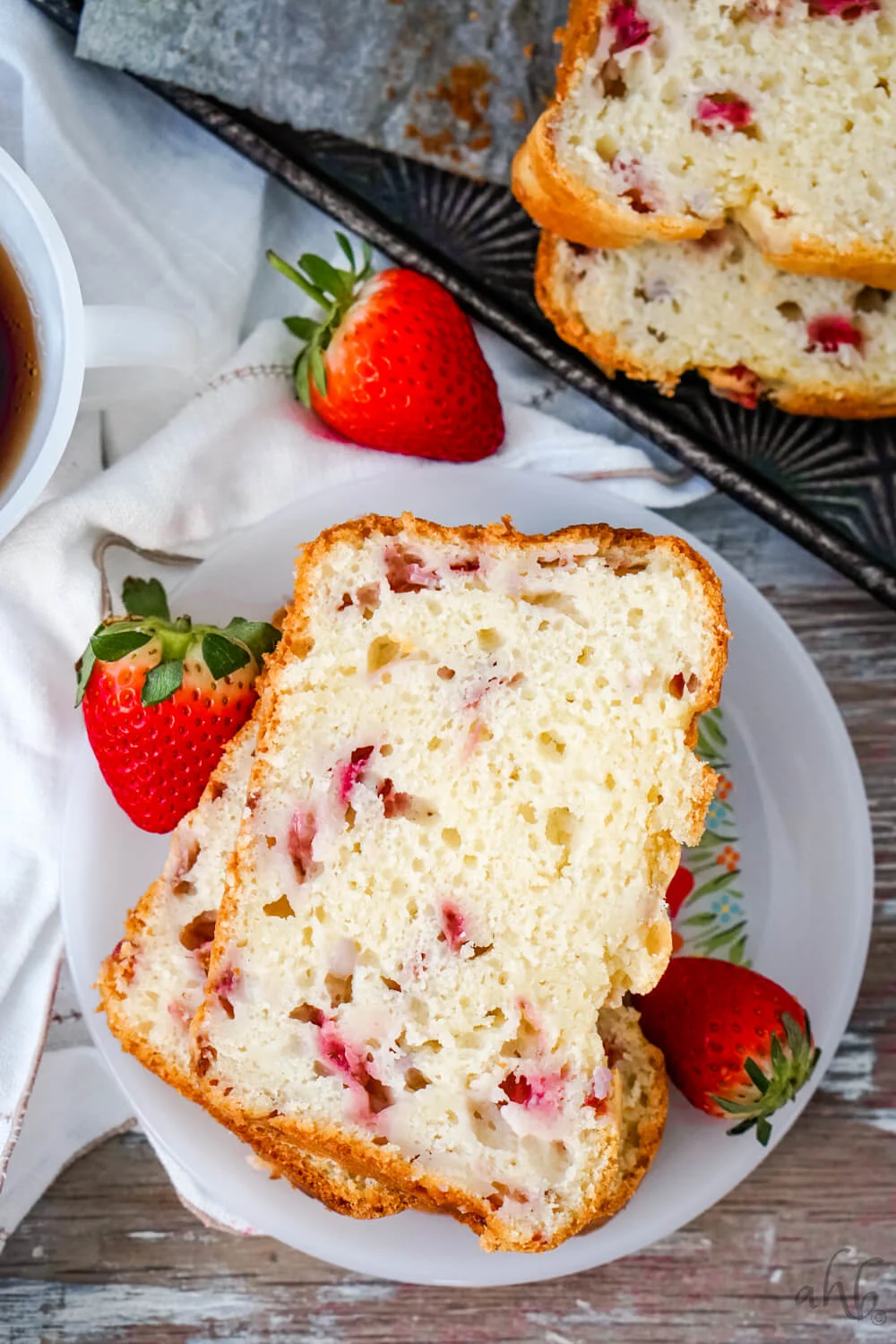 Two Slices of Strawberry Bread on a white plate surrounded by fresh strawberries. 