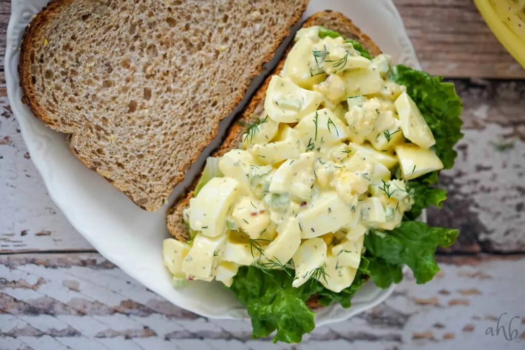 An open face egg salad sandwich on a white plate. 