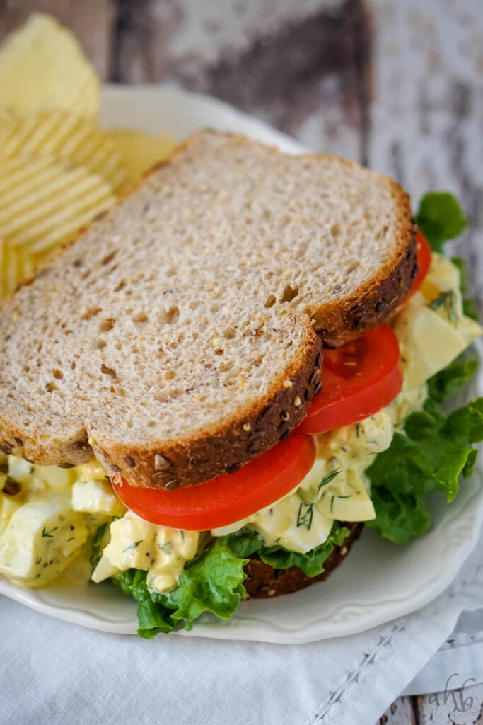 A homestyle egg salad sandwich with lettuce and tomato on a white plate. 