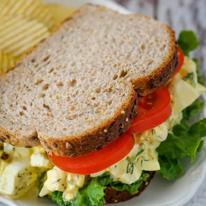 A homestyle egg salad sandwich with lettuce and tomato on a white plate.