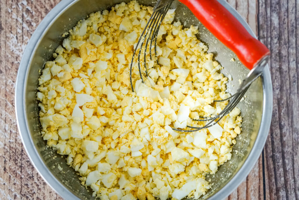 a bowl of chopped hard boiled eggs with a pastry blender to one side. 