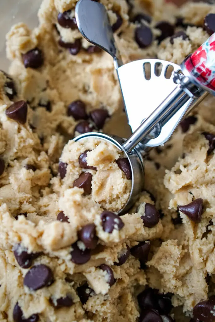 A mixing bowl full of chocolate chip cookie dough with a cookie scoop. 