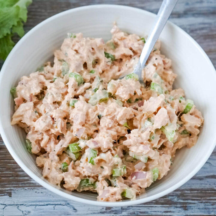 A white bowl full of buffalo tuna salad with a plate of lettuce leaves to one side.