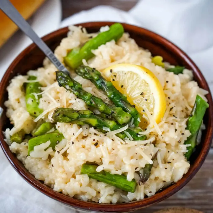 A brown bowl full of Instant Pot Asparagus Risotto, garnished with asparagus spears and a slice of lemon.
