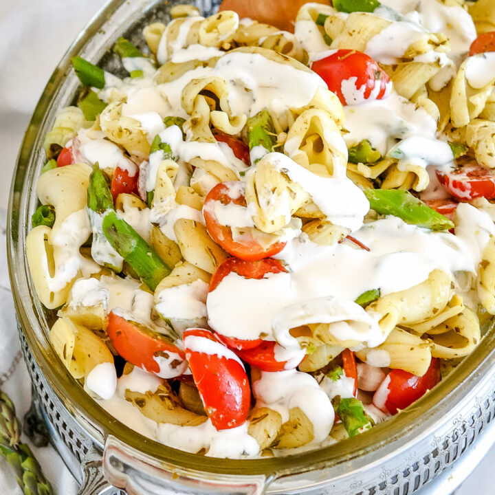 A serving dish of creamy pesto pasta salad drizzled with homemade creamy dressing.