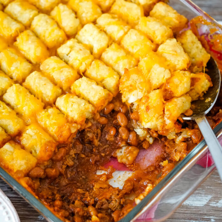 A close up image of a pan of pulled pork tater tot casserole with a serving spoon dishing out a helping.