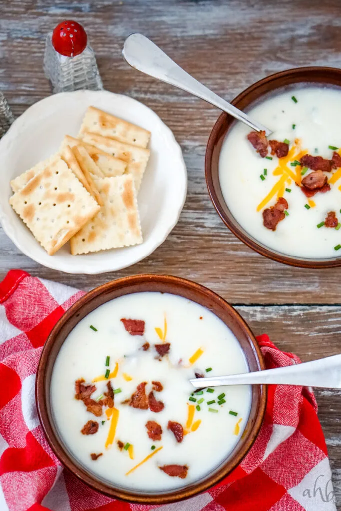 Two bowls of 4 ingredient potato soup with a white bowl of saltine crackers.