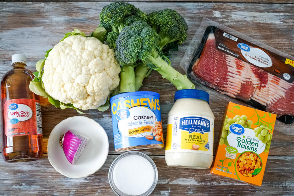 The ingredients needed to make Amish Broccoli Cauliflower salad: Apple cider vinegar, cauliflower, broccoli, bacon, red  onion, sugar, cashews, mayo, and golden raisins