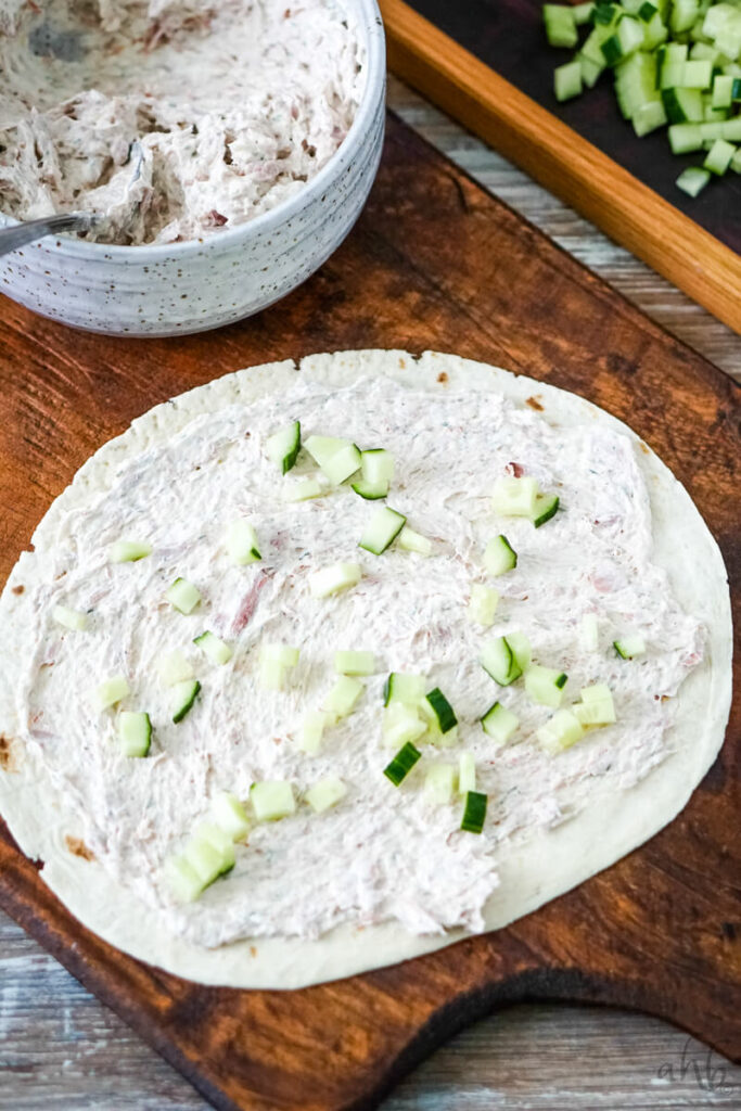 The tuna mixture is evenly spread onto a flour tortilla and is topped with diced cucumbers. 