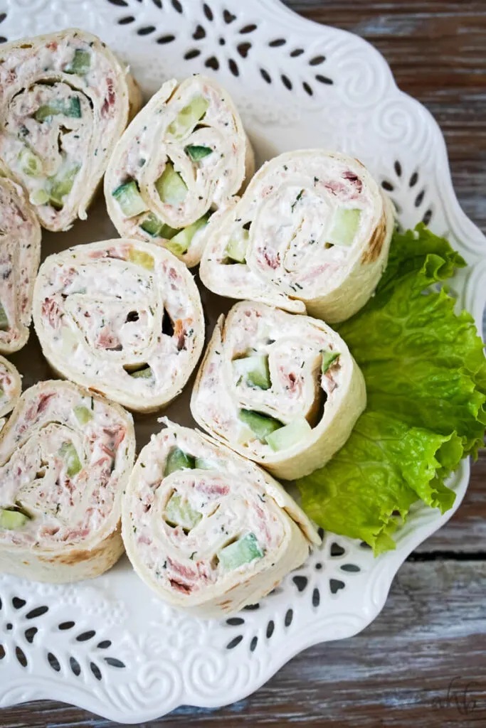 A plate of white pinwheels on a bed of lettuce served on a decorative white plate.