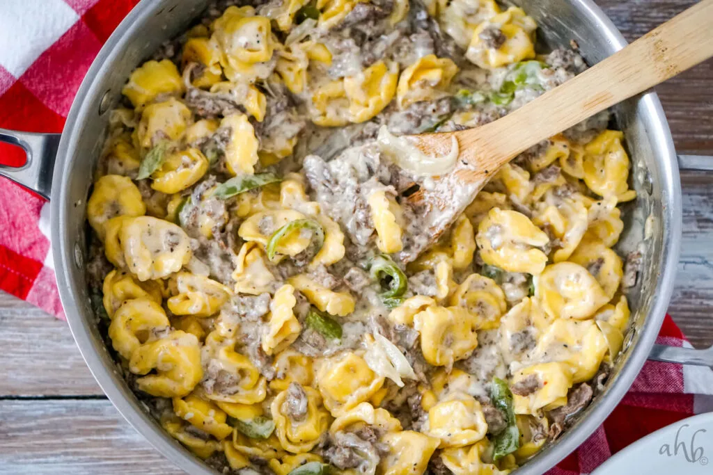 A wooden spoon sits in the sauté pan with the Philly Cheesesteak Tortellini.
