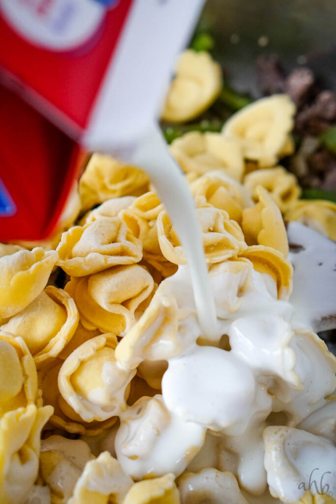 The frozen tortellini and heavy cream are added to the pan.