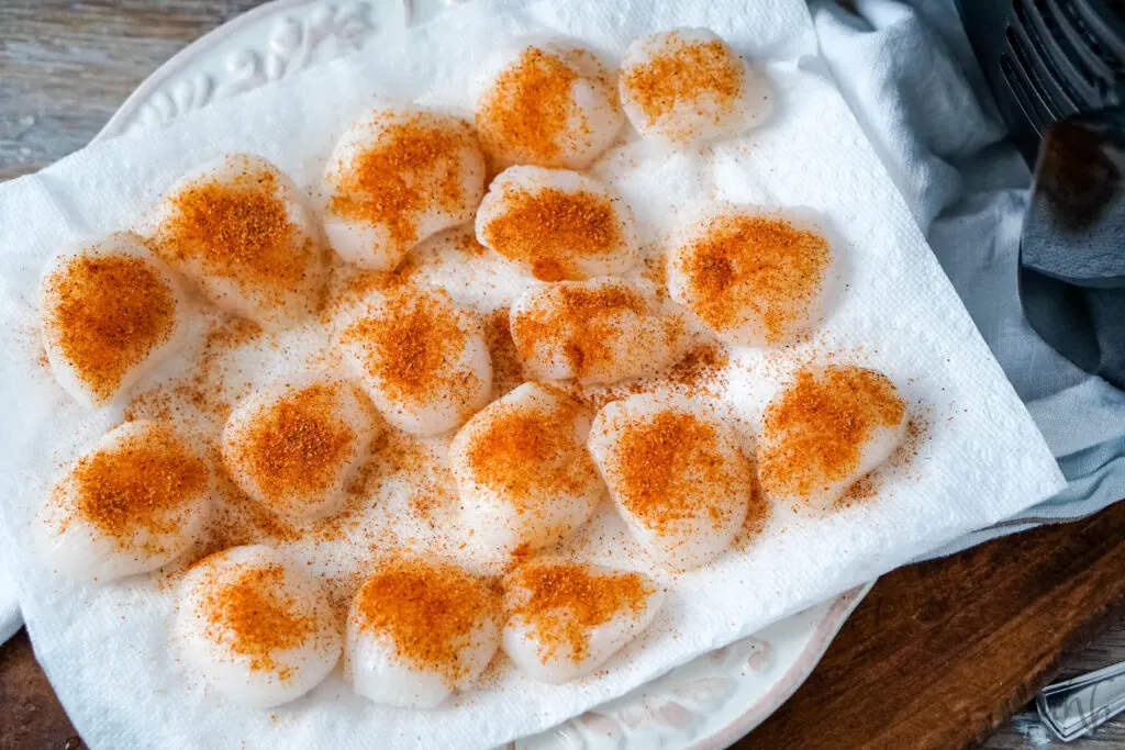 Cajun seasoning is added to the scallops sitting on a paper towel on a paper plate.