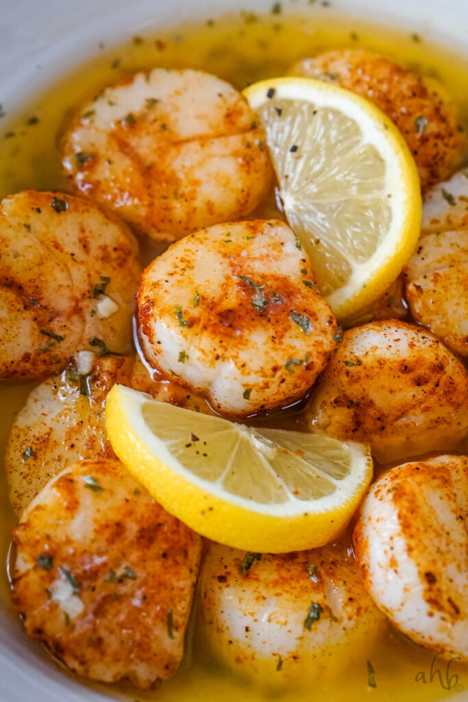 Completed scallops are tossed in garlic butter and served with lemon slices.