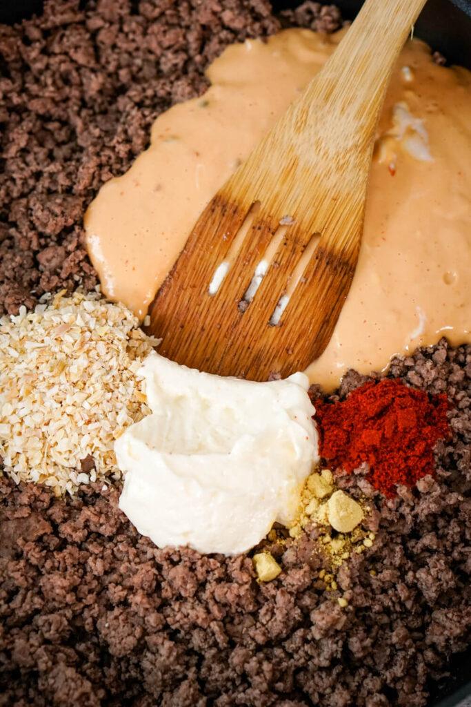 A wooden spoon combines browned ground beef, thousand island dressing, dried minced onion, mayo, dried ground mustard, and paprika.
