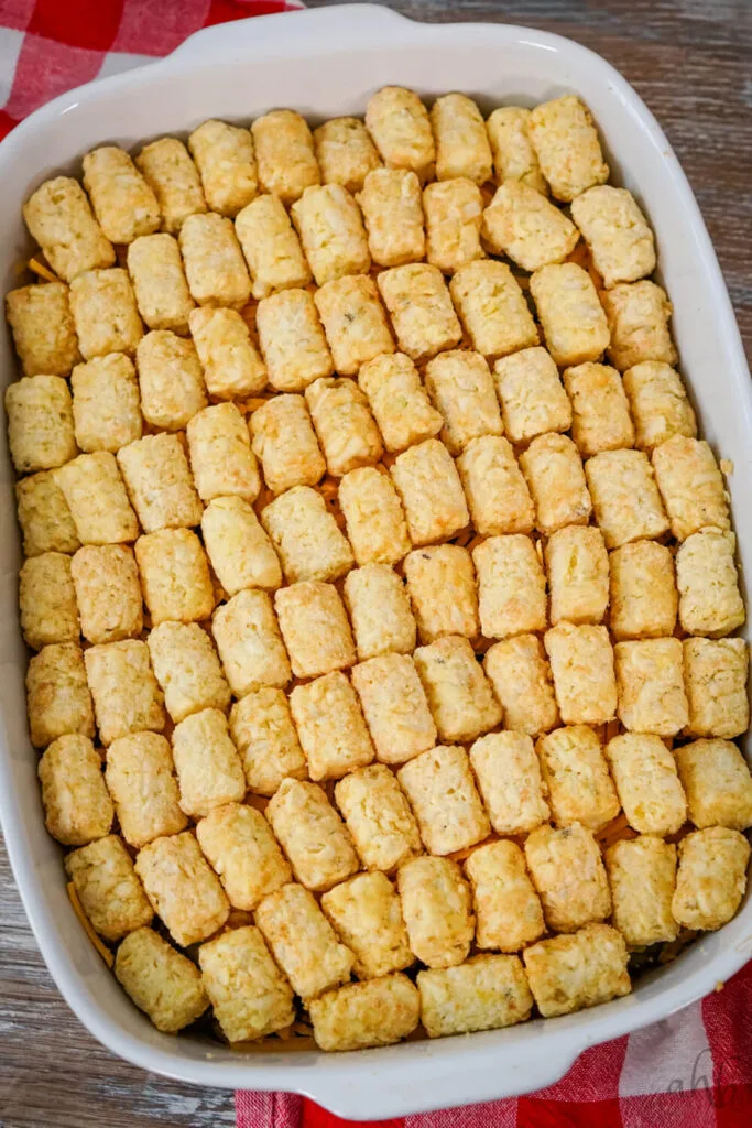 Ground beef, pickles, and shredded cheddar are topped with tater tots in a white baking dish.