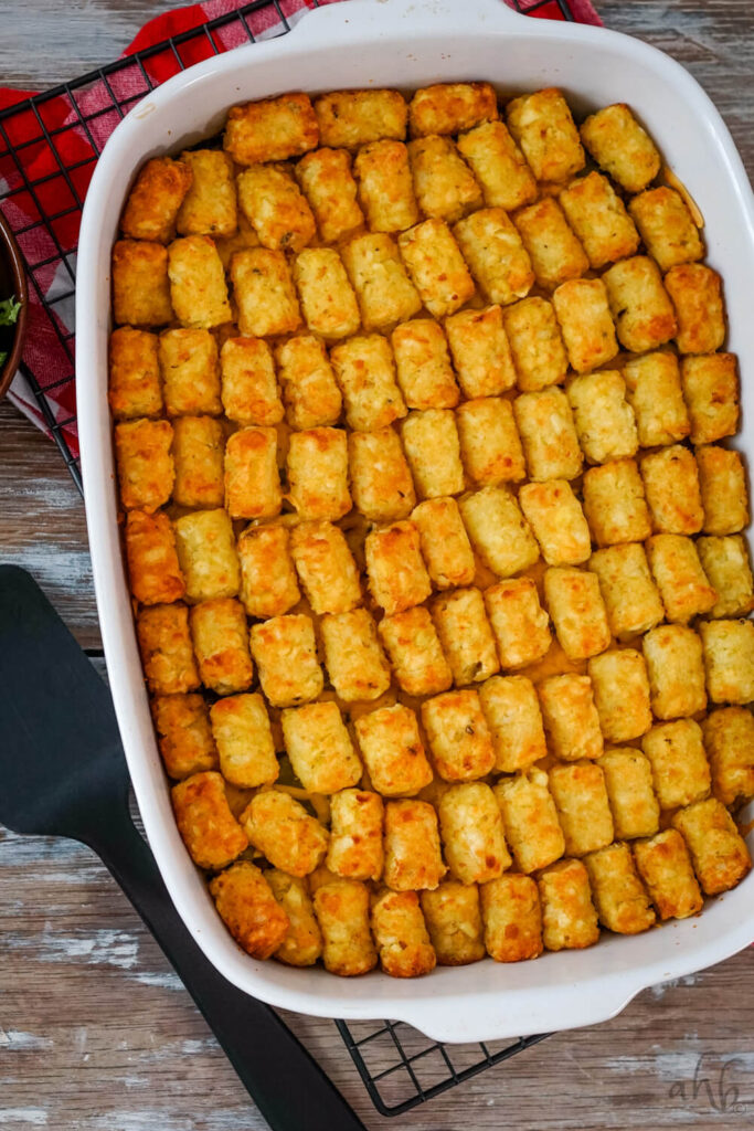 The freshly baked casserole with golden brown tater tots sits on a black cooling rack.
