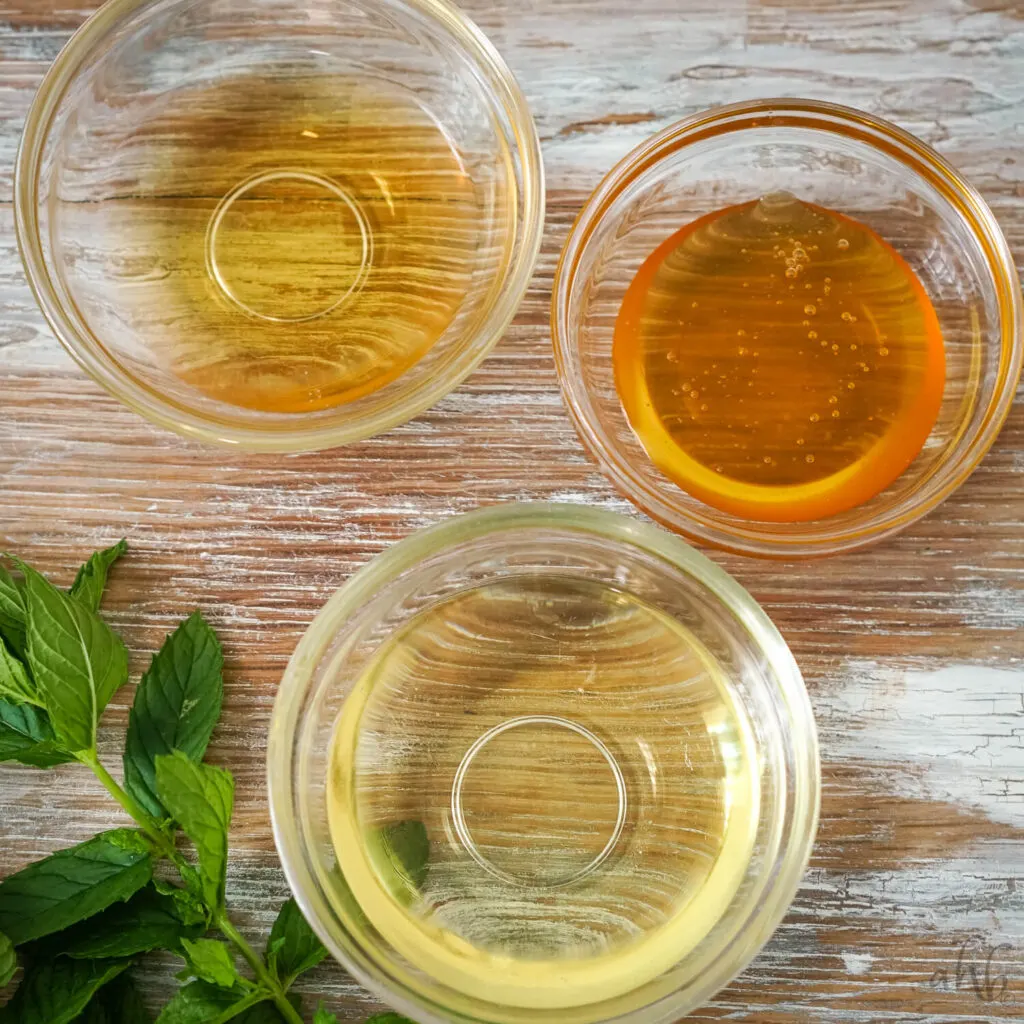Three clear bowls of vegetable oil, honey, and apple cider vinegar.