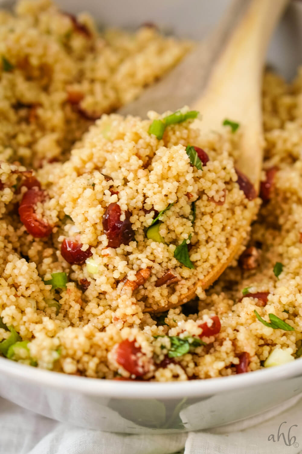 A wooden spoonful of cranberry couscous salad in a white bowl.