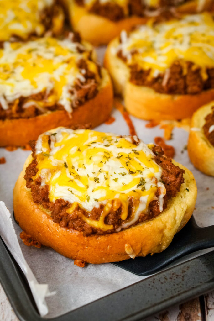 A Garlic Bread Sloppy Joe being scooped off of a baking sheet with a black spatula.