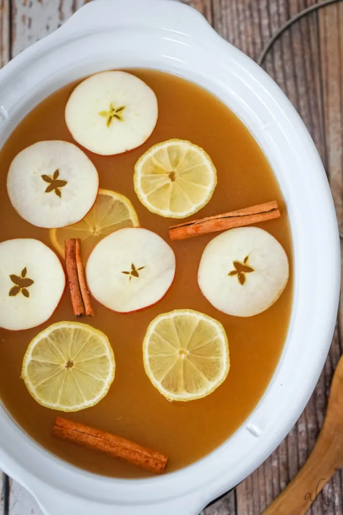 Lemonade Cider in a white crockpot with sliced apples, lemons and cinnamon sticks floating on top.