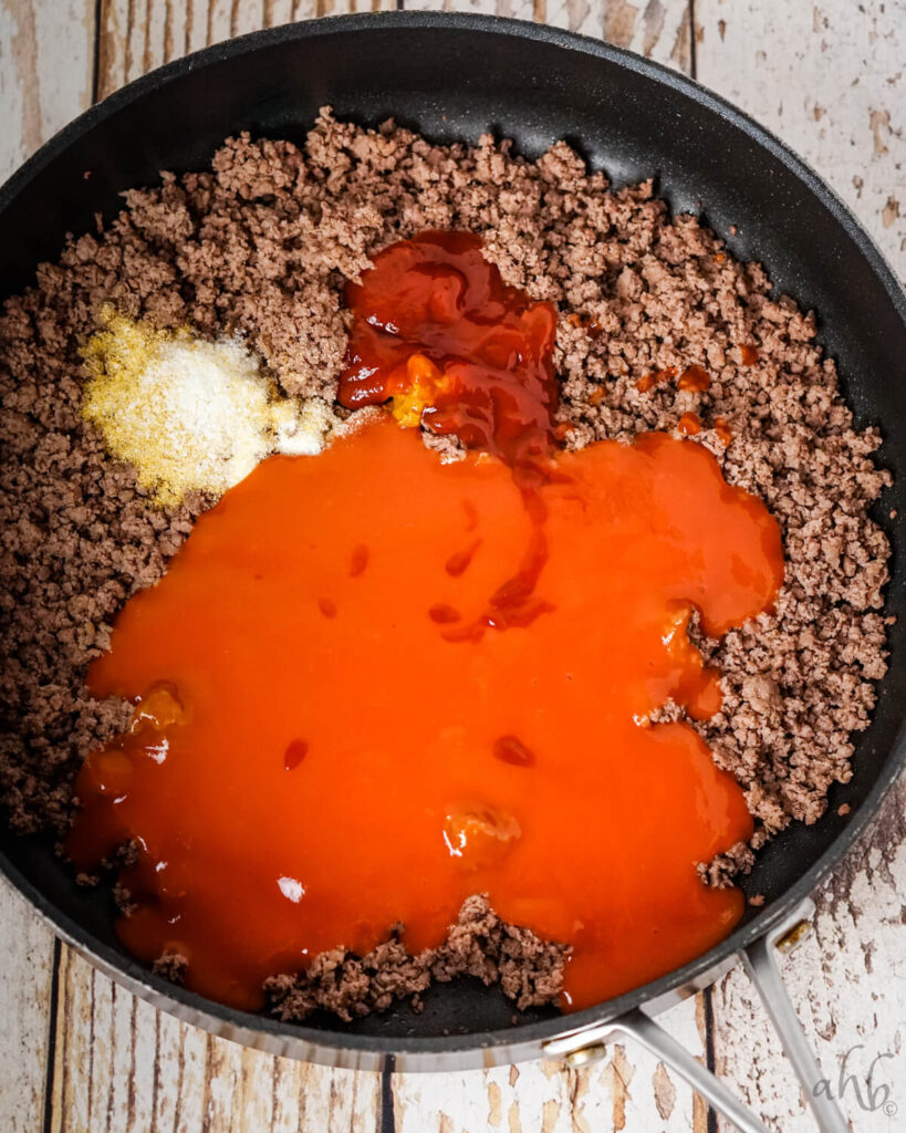 Tomato soup, Worcestershire sauce, yellow mustard, and ketchup, onion powder, salt, and garlic powder, and browned ground beef sitting in a medium black skillet.