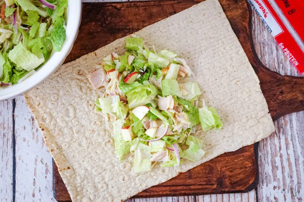 The mix is laid out in the center of a large tortilla on a wooden cutting board.