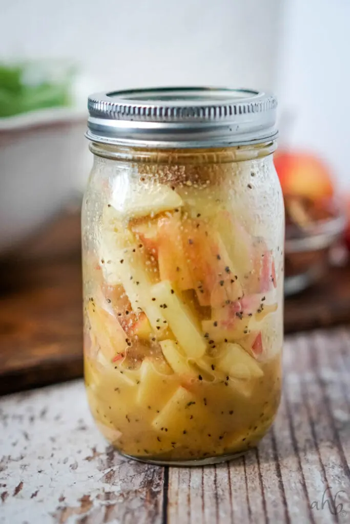 A mason jar of homemade maple vinaigrette filled with thinly sliced apples.