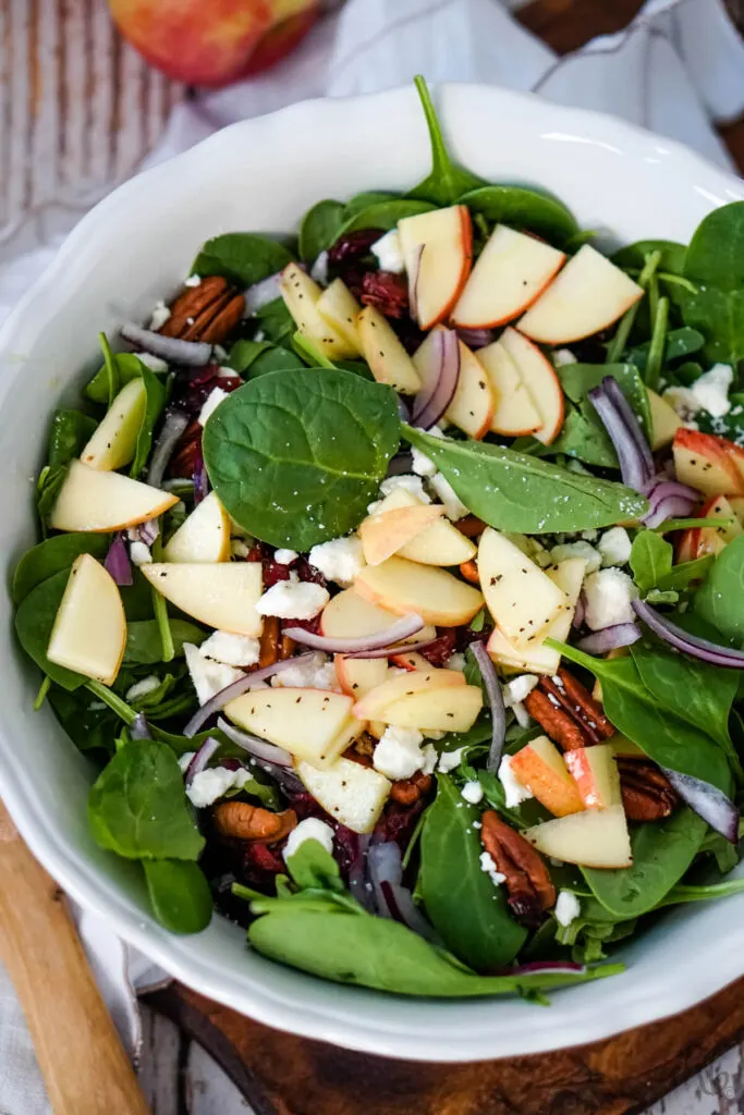 A white bowl filled with Apple Feta Spinach Salad.