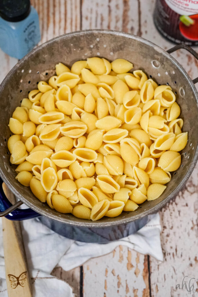boiled and drained shell pasta in a colander on top of a blue stockpot.