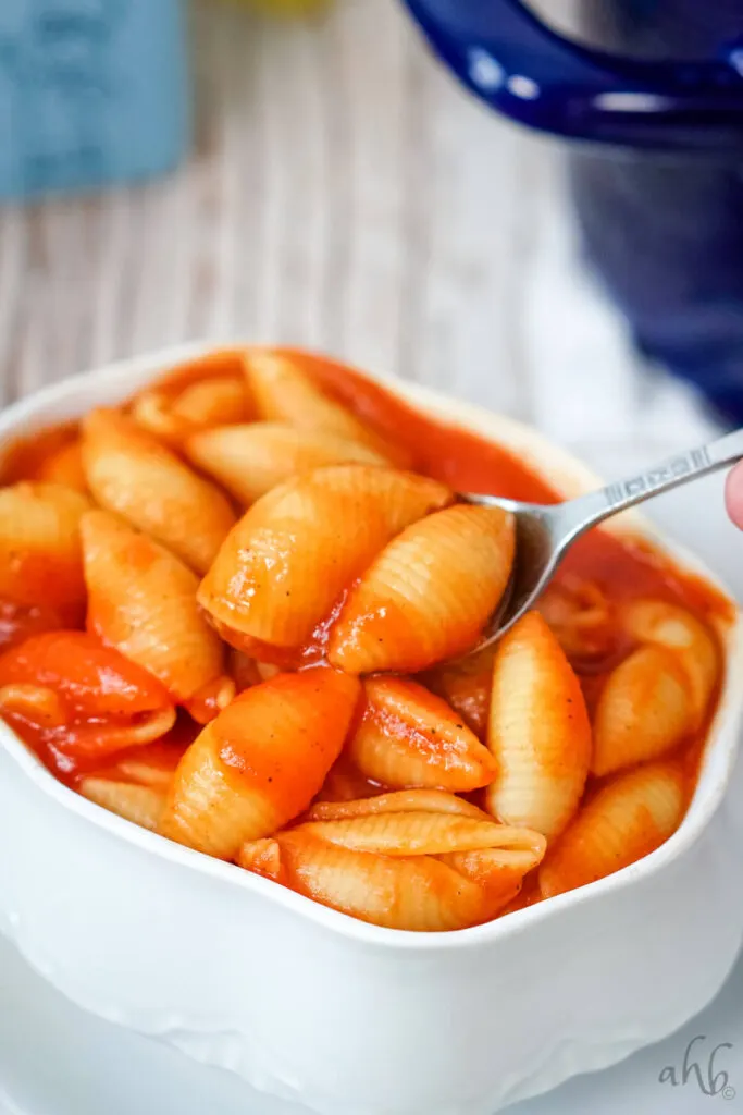 A serving of Old Fashioned Tomato Macaroni in a white bowl being scooped with a spoon.